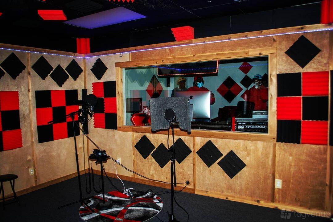 A recording studio with a vocal booth, acoustic foam panels, and a large control room window at Industry Wave Studio.