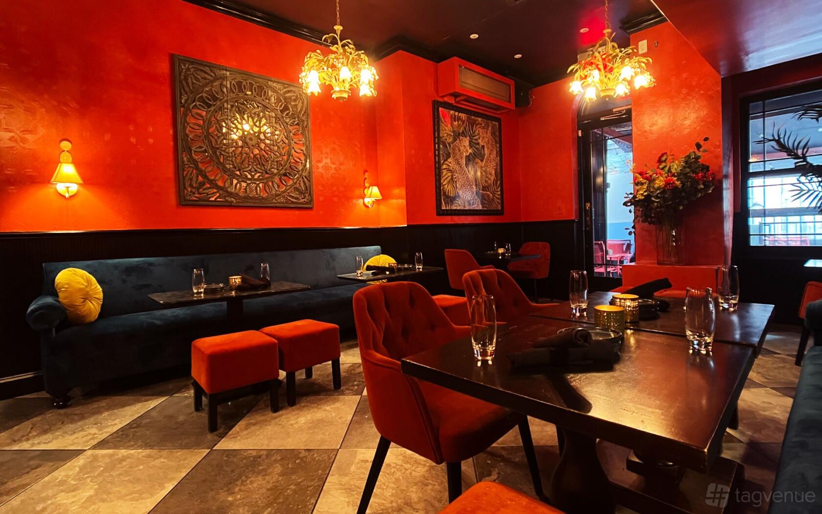 A cocktail bar with red walls, velvet seating, ornate chandeliers, and decorative wall art at BIXI.
