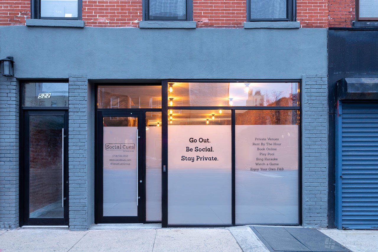 A versatile event space with glass storefront, marquee lights, and brick facade at Social Cues - Vogue.