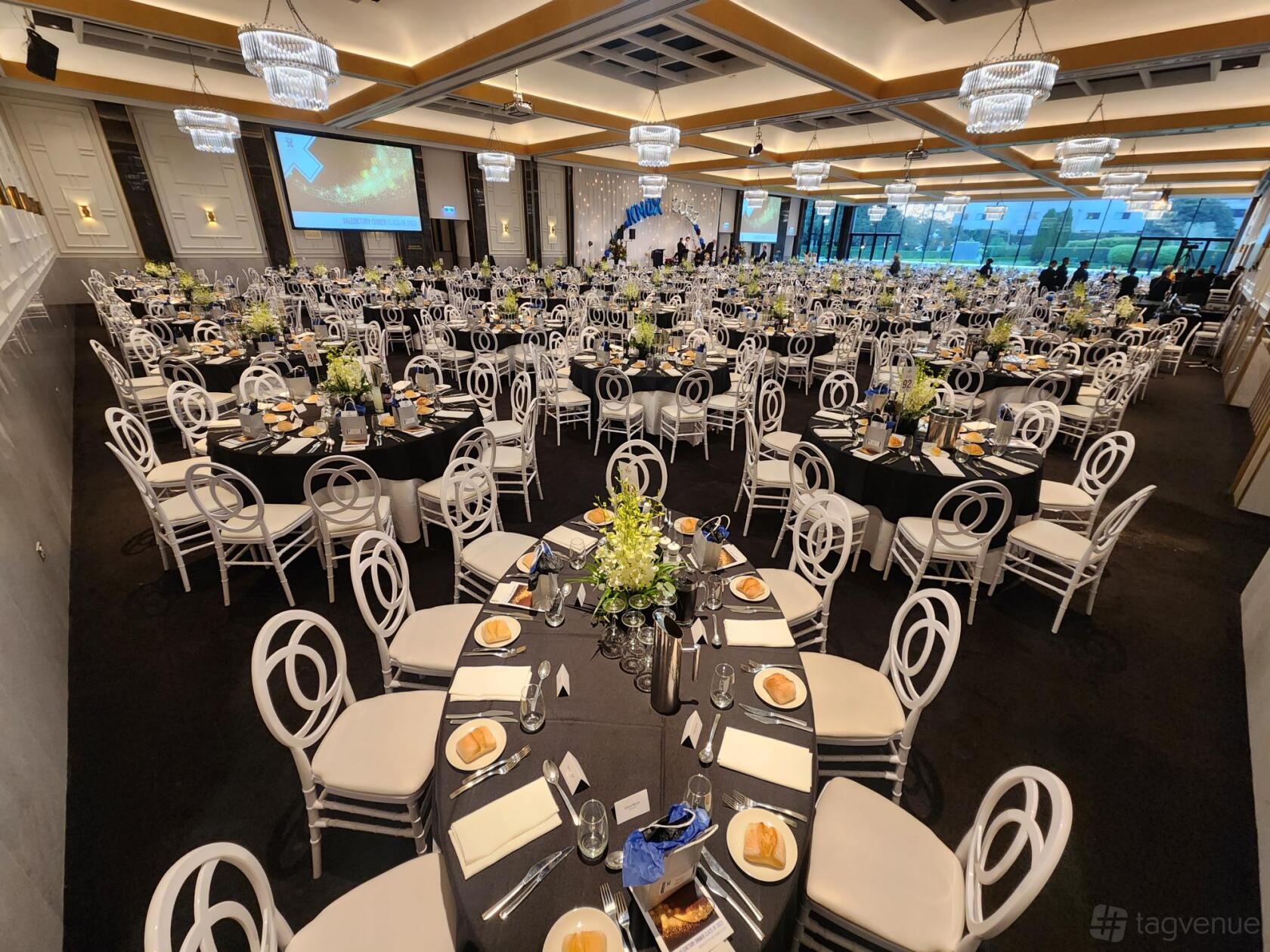A ballroom with round tables dressed in black linens, white chairs, chandeliers, and floor-to-ceiling windows at Miramare Gardens.
