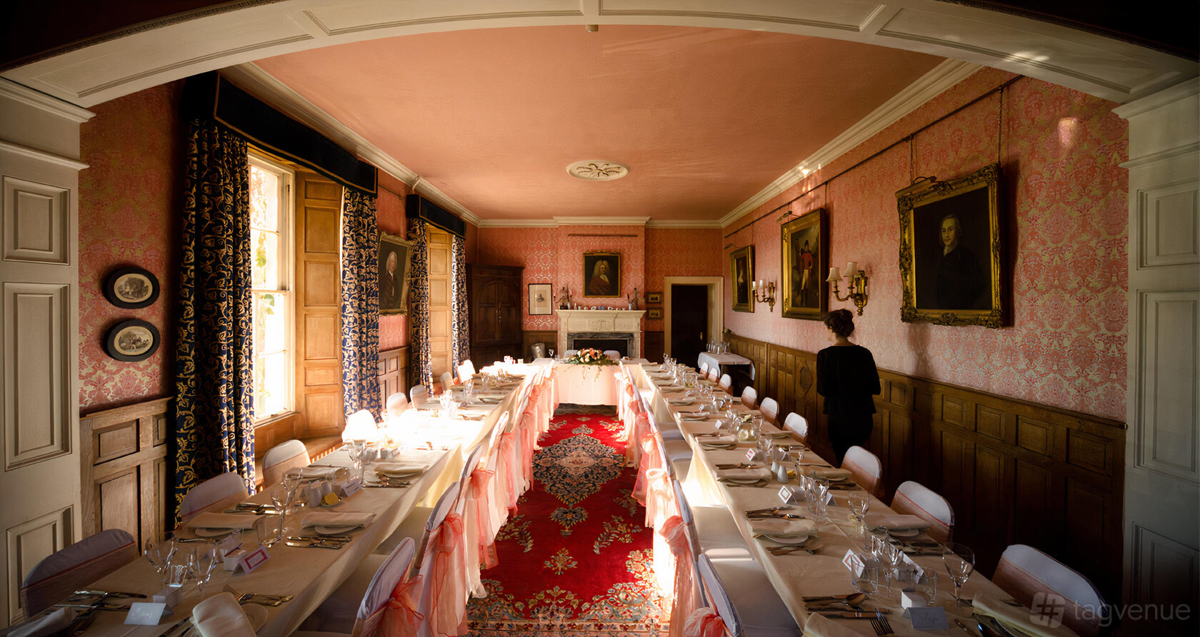 A country house with long banquet tables, ornate wallpaper, large windows, and framed portraits at Low House.