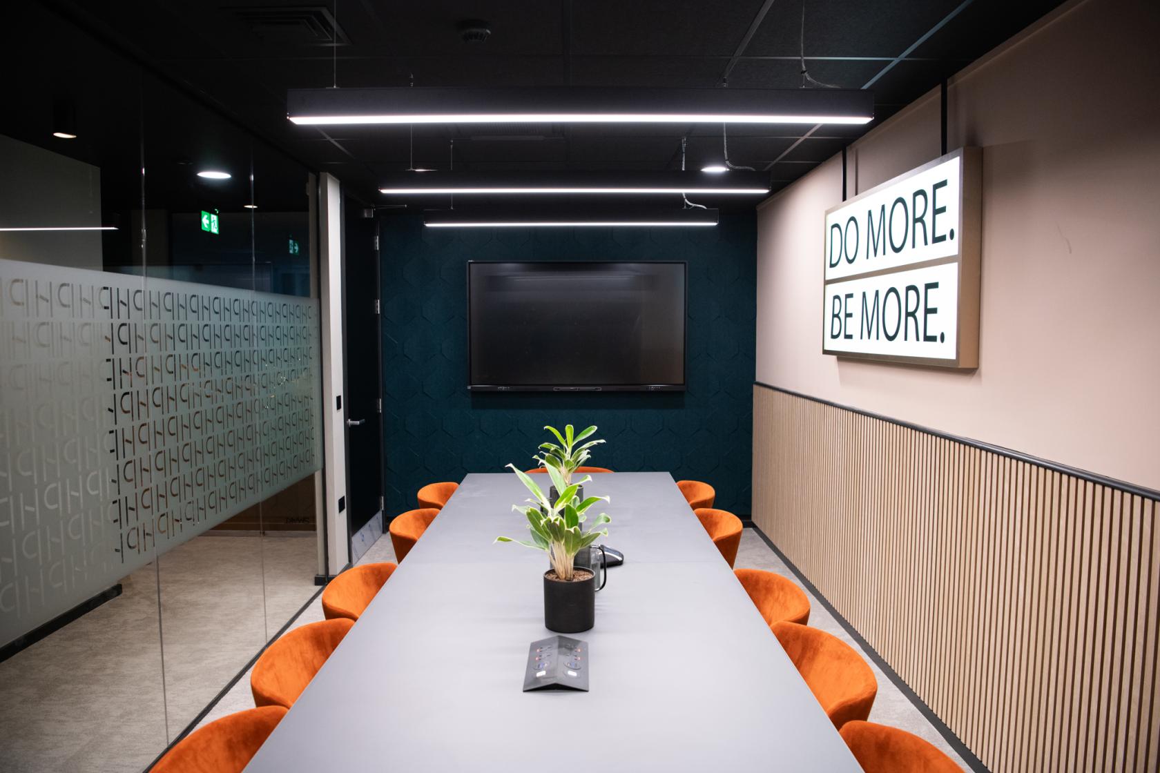 A meeting room with a long table, orange chairs, wall-mounted TV, and motivational signage at Wizu Workspace - Newcastle - Portland House.