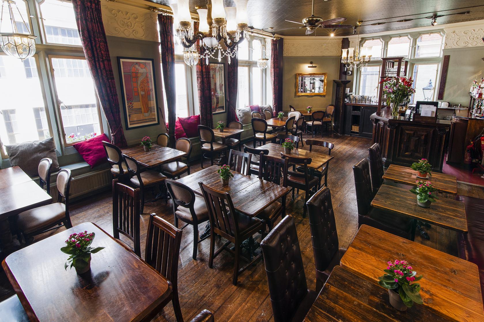 A dining room with vintage wooden tables, chandeliers, and large windows with velvet curtains at Clachan.
