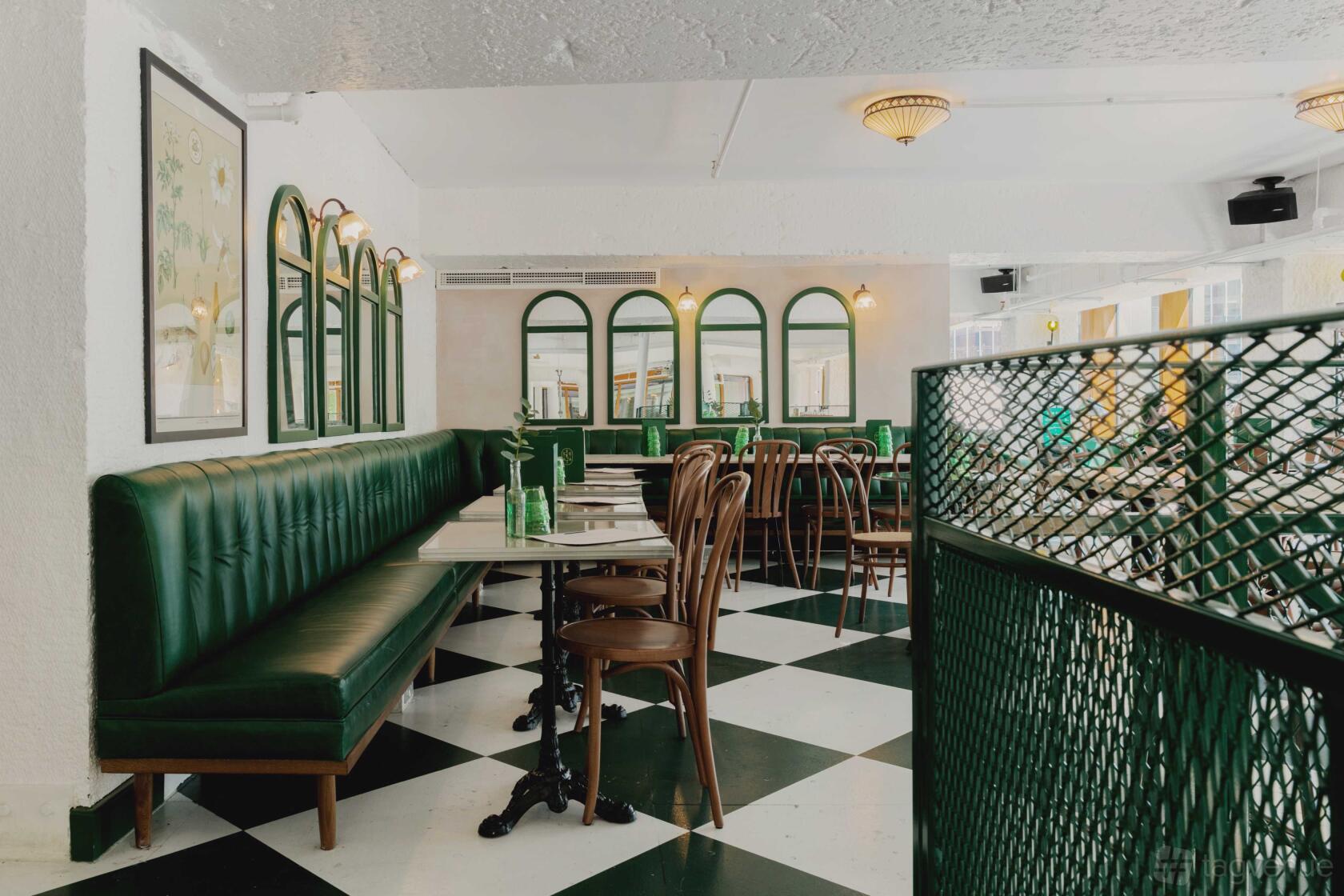A dining room with green upholstered banquette seating, wooden chairs, and black-and-white checkered floors at Serata Hall.