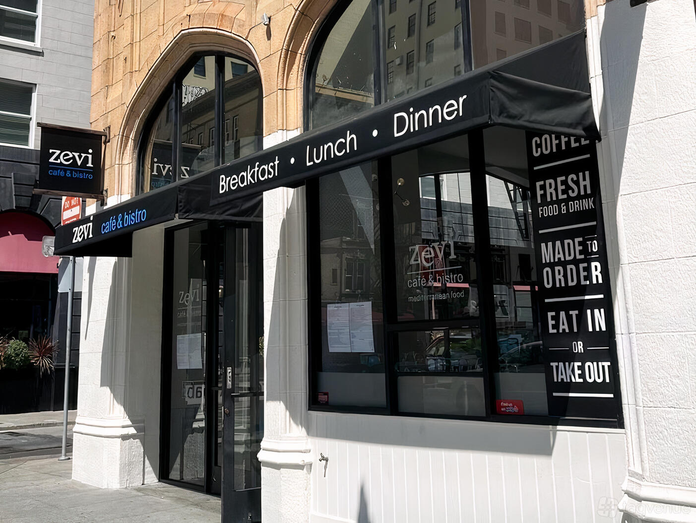 A café with large arched windows and black awnings reading breakfast, lunch, and dinner at Zevi Cafe & Bistro.