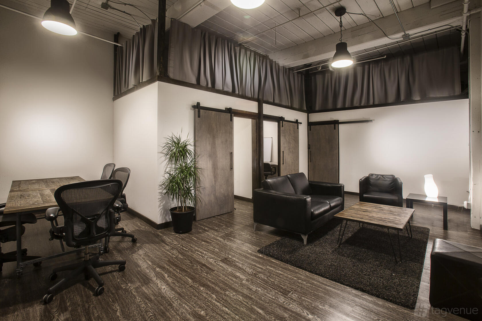 A photo studio with high ceilings, dark wood flooring, black leather seating, and sliding barn doors at Studio G Seattle.
