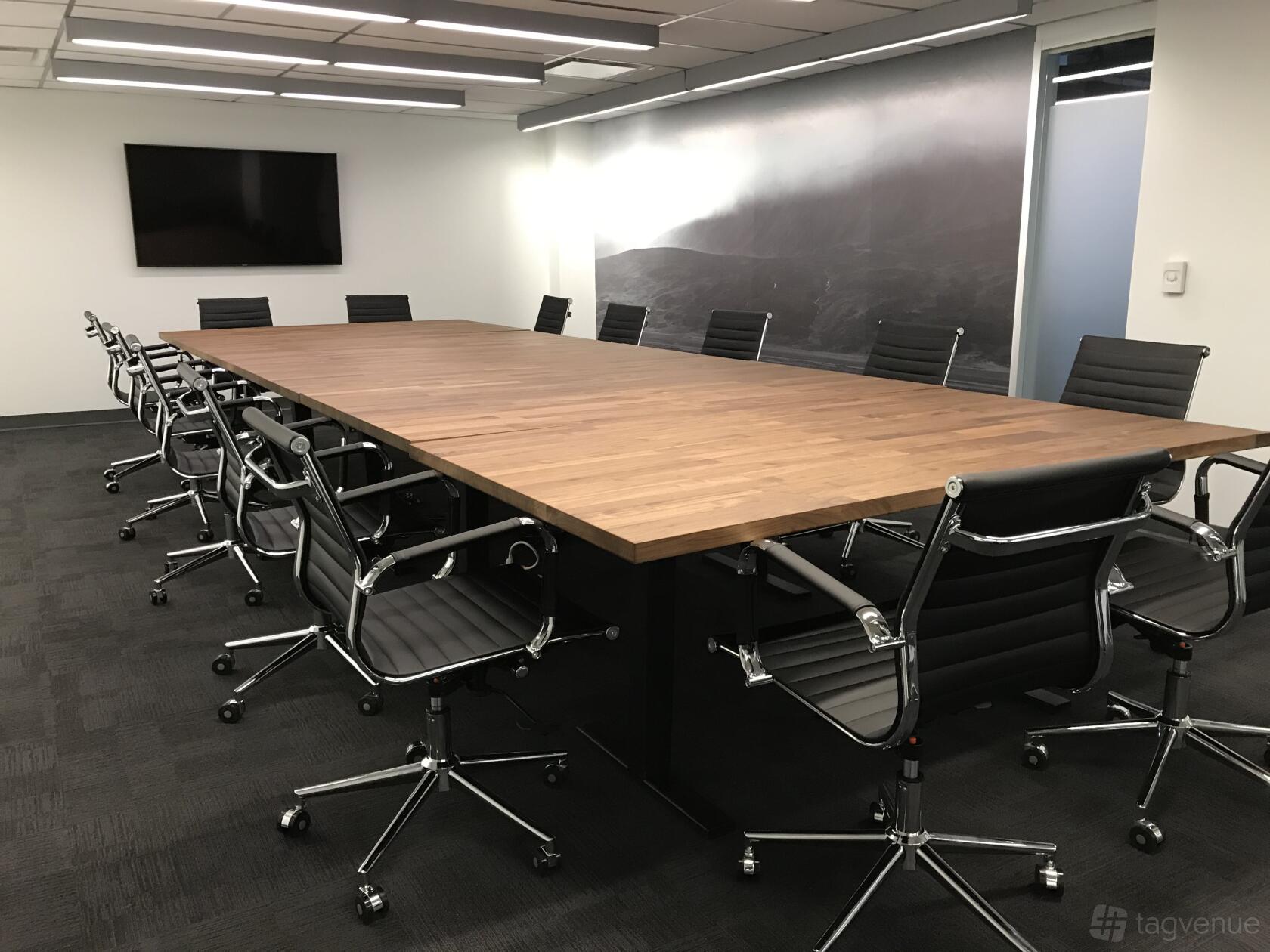 A boardroom with a large wooden conference table, black leather chairs, and a wall-mounted TV at Adelaide House Coworking.