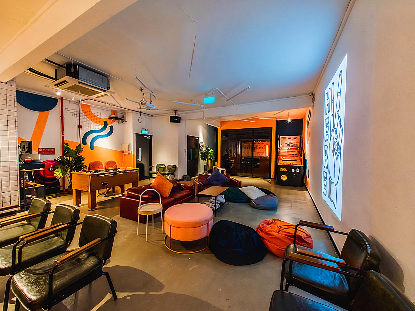 An event venue with eclectic seating, colorful wall art, bean bags, and a large projection screen at HERE.