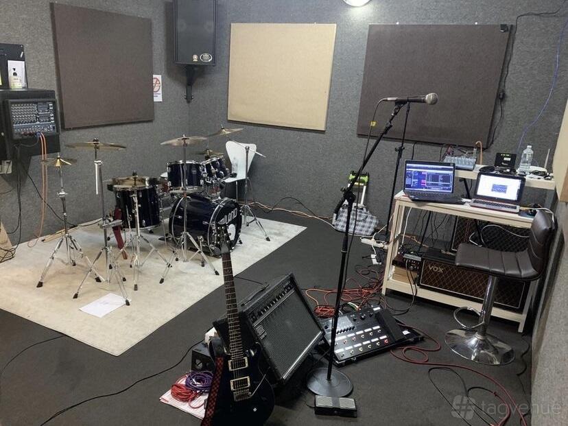 A rehearsal room with a drum kit, guitar, microphone, sound mixing equipment, and acoustic panels at Bayside Rehearsal Studios.