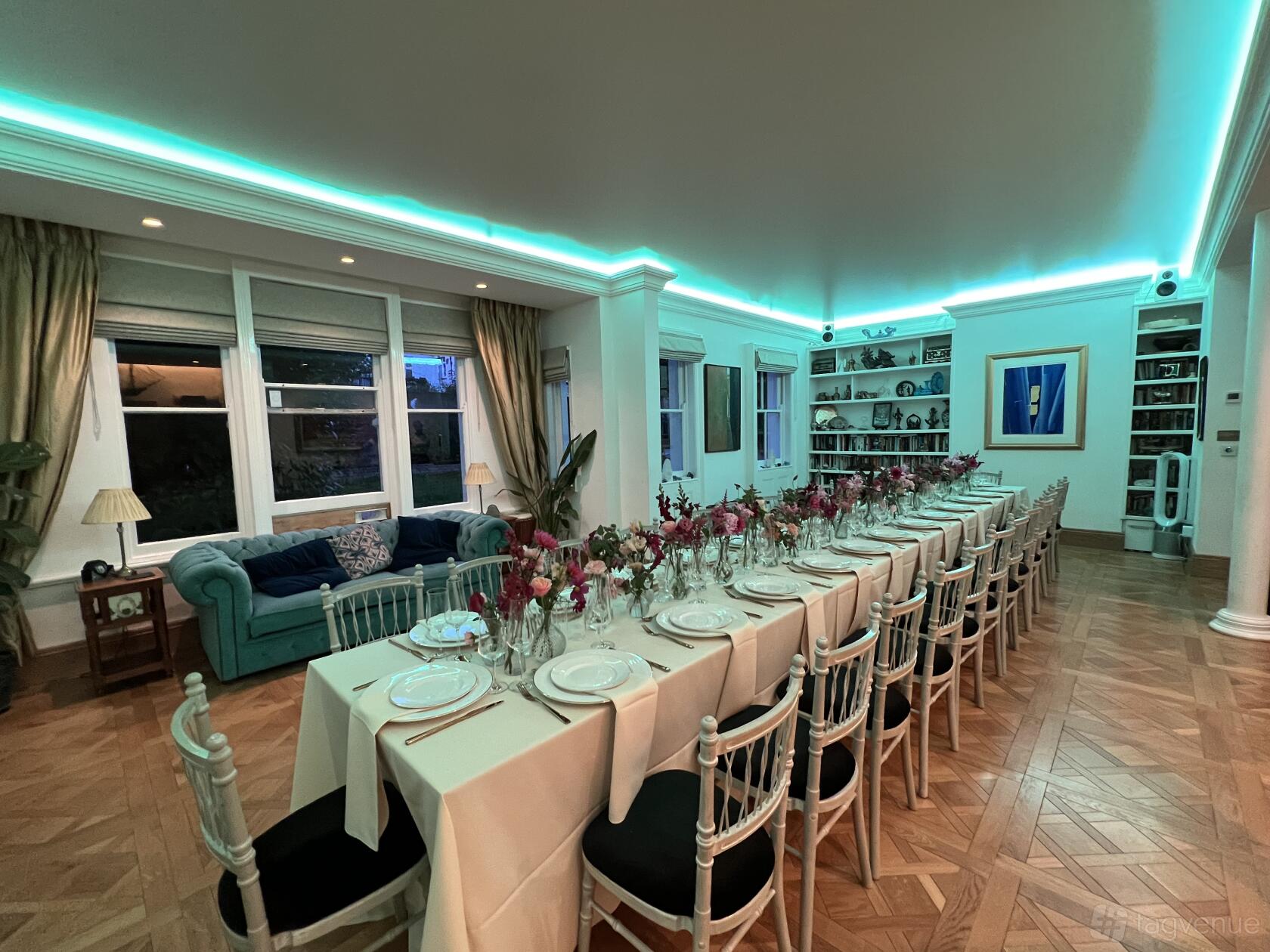 A dining room with a long banquet table, floral centerpieces, parquet flooring, and LED ceiling lighting at Urban Oasis North London.