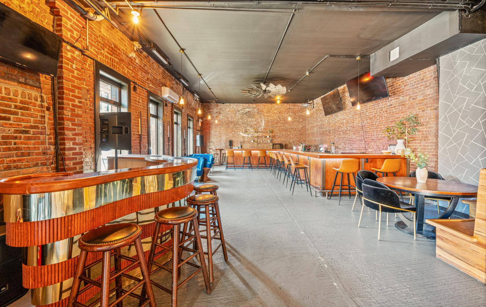 A bar with exposed brick walls, brass-accented counter, wooden stools, and lounge seating at Saint James - Luxe Lounge.