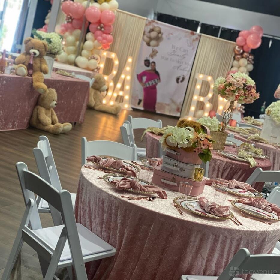 An event venue with round tables covered in pink velvet linens, floral centerpieces, and large teddy bears at I AM Studios.