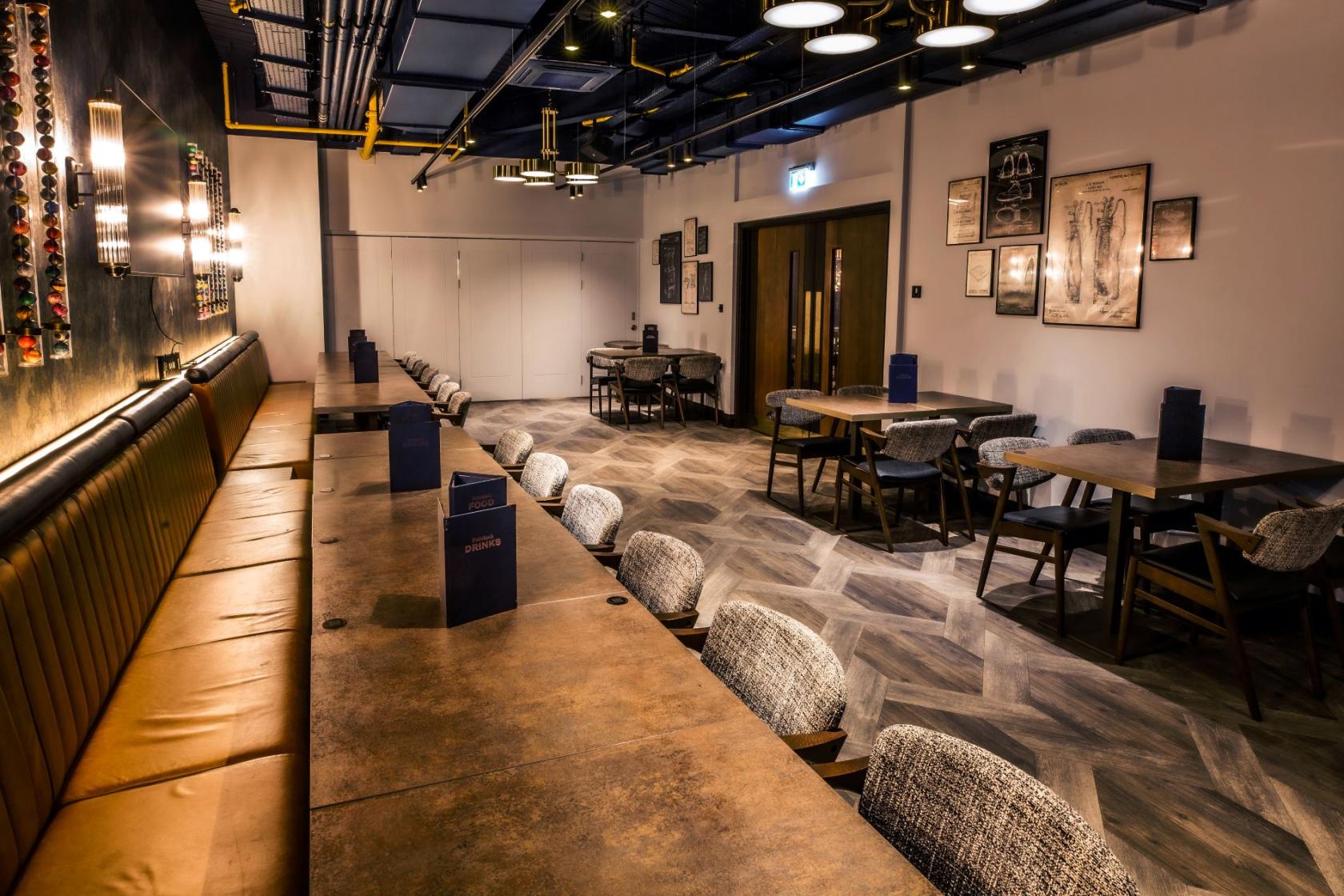 An event venue with long banquette seating, wall sconces, and framed prints at Puttshack Watford.