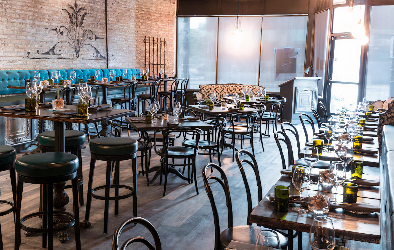A restaurant dining room with exposed brick walls, teal banquette seating, and tables set with glassware at Uvae Kitchen & Wine Bar.