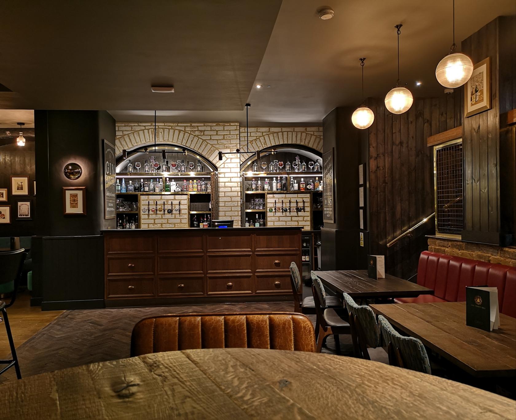 A function room with a brick arch bar, hanging globe lights, leather chairs, and red banquette seating at The Trinity Bell.