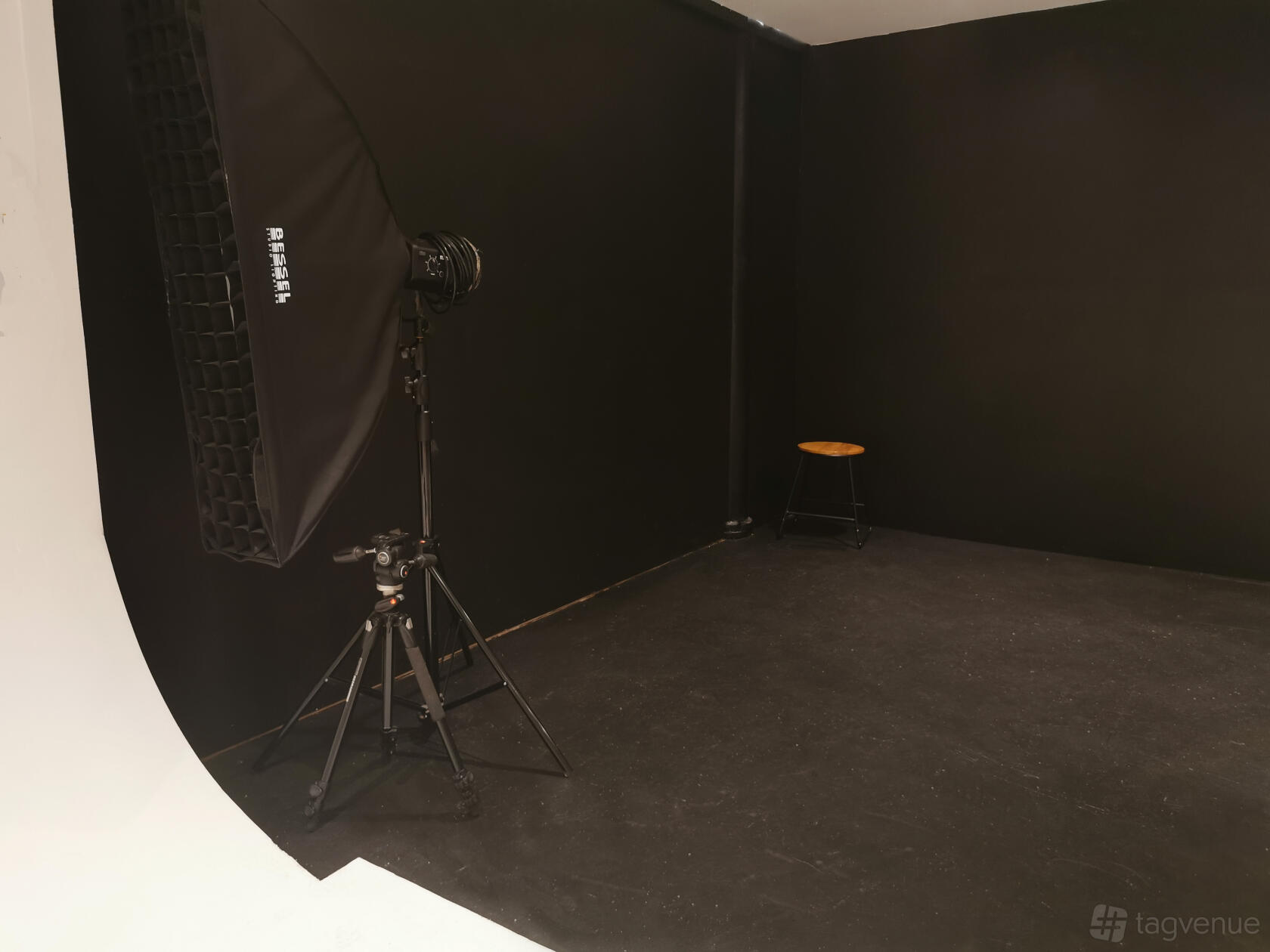 A photo studio with a black infinity cove, a lighting softbox on a stand, and a wooden stool at Montrose Studios.