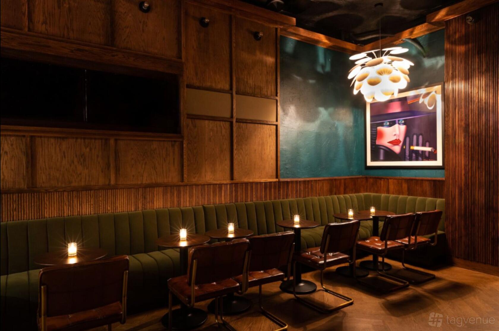 A cocktail bar with a green upholstered banquette, small candlelit tables, wood-paneled walls, and modern artwork at J.Bespoke.