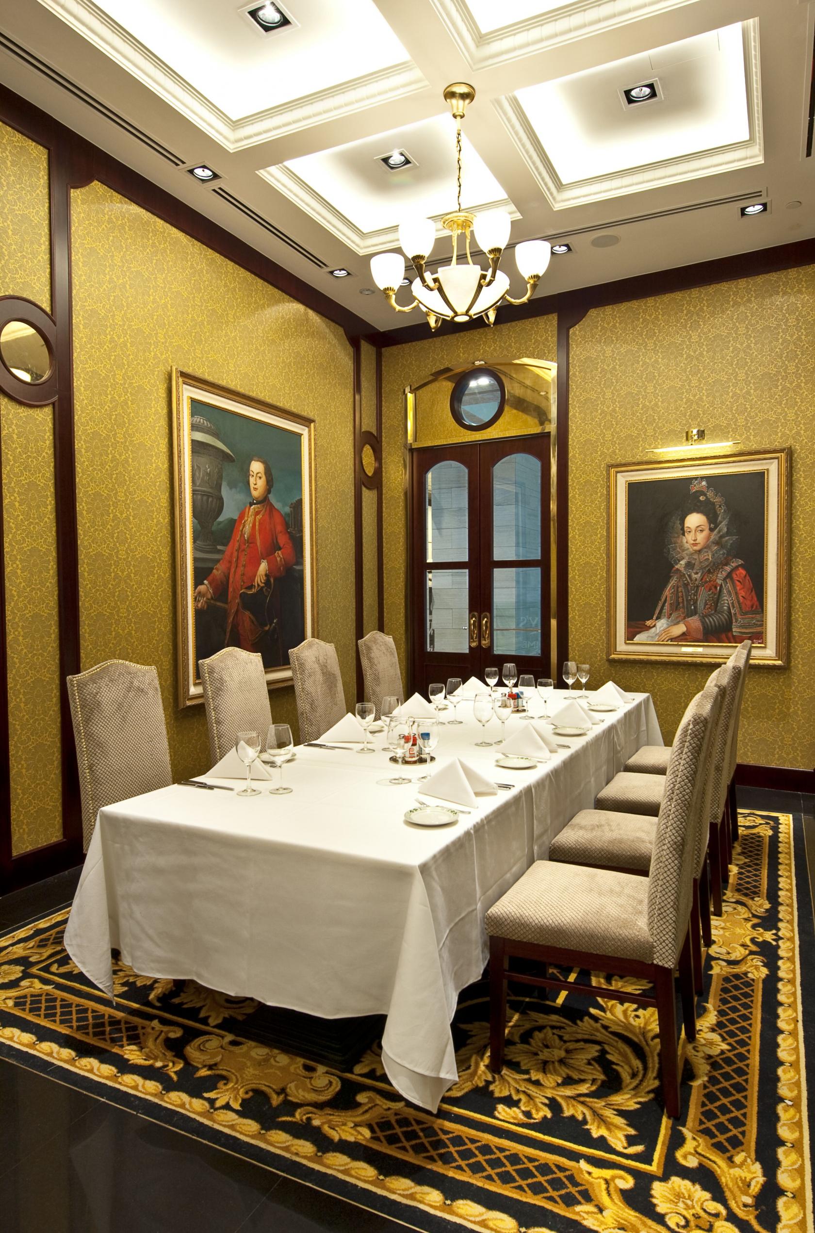 An event space in a restaurant with a long table set for dining, upholstered chairs, and classic portraits at Lawry's The Prime Rib.
