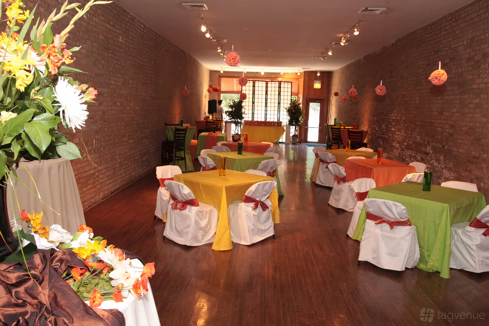 An event venue with exposed brick walls, round tables covered in colorful linens, and wooden floors at Room43.