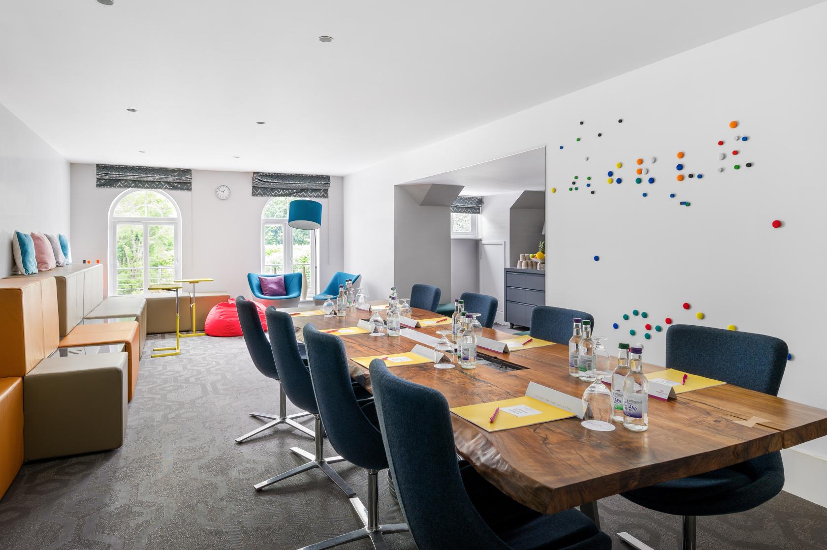 An event space with a wooden boardroom table, colorful seating, whiteboard wall, and natural light at Crowne Plaza Gerrards Cross.