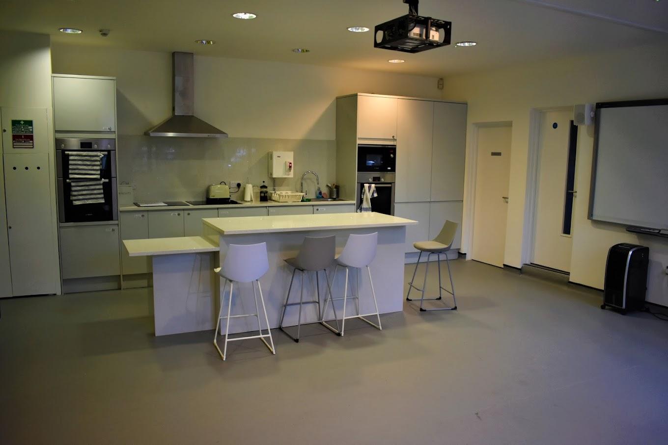 A community centre kitchen with a central island, modern appliances, and bar stools at Castlehaven Community Centre & Hub.