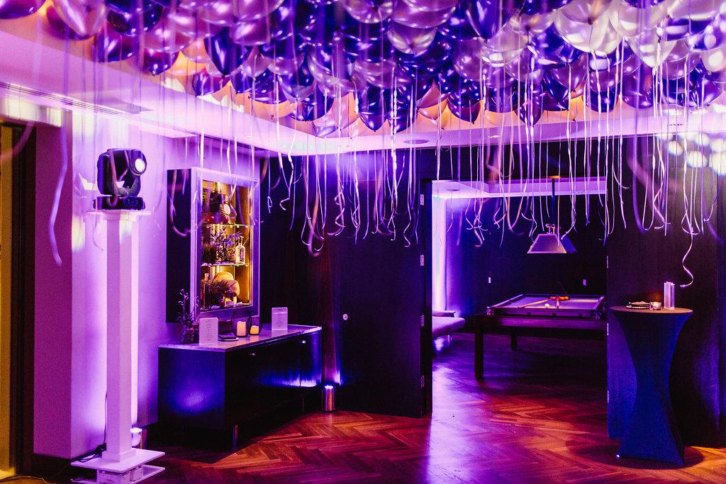 A hotel event room with a ceiling of purple balloons, hardwood floors, and a billiards table at South Place Hotel.
