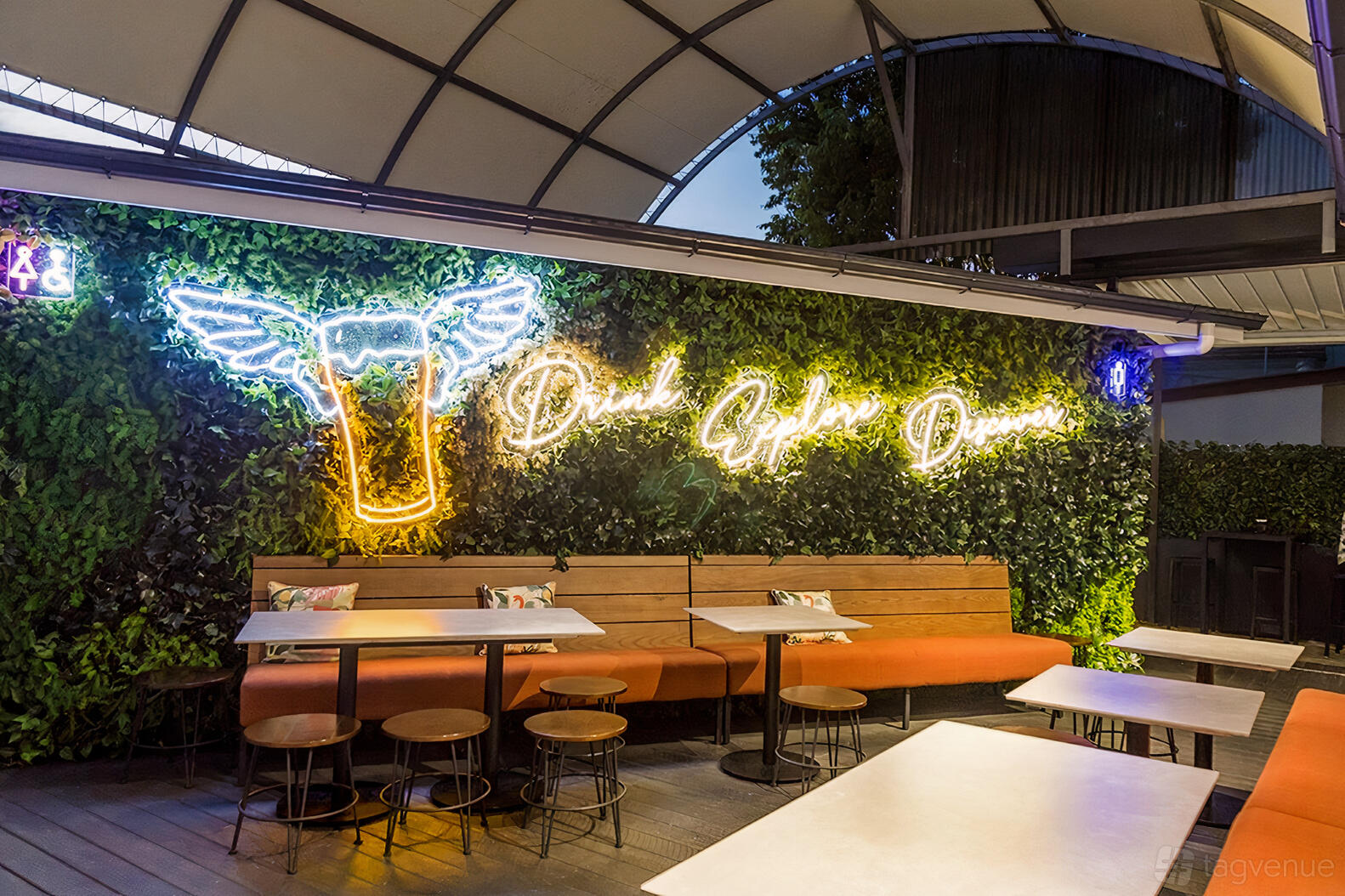 An event space in a pub with a green plant wall, neon beer sign, long bench seating, and canopy at Sandgate Post Office Hotel.