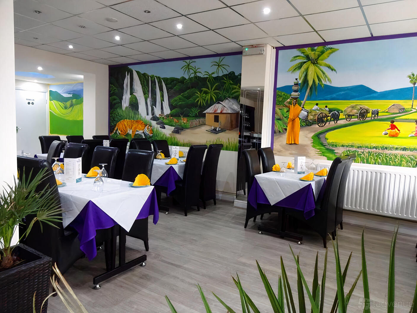 A restaurant with colorful mural walls, white tablecloths, and black chairs at Rumana's.