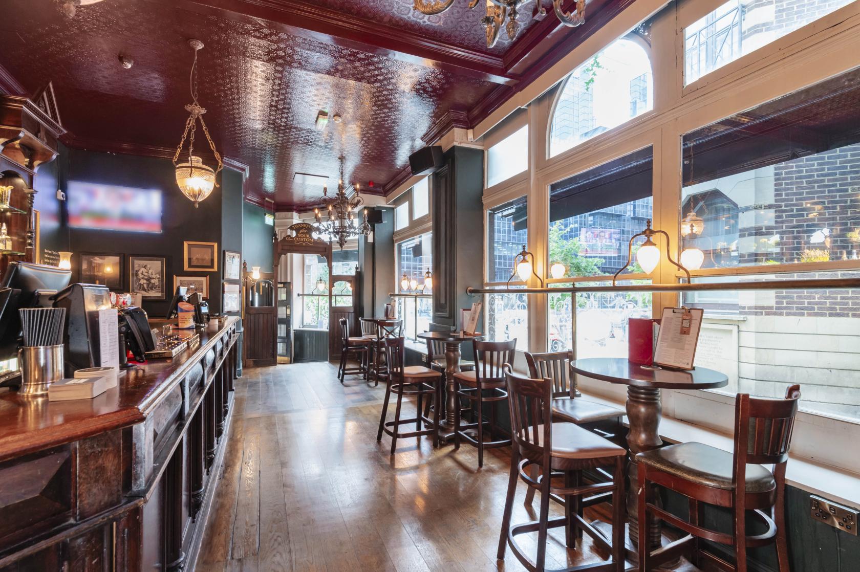 A pub with wooden floors, round tables, high-backed chairs, and large street-facing windows at The Walrus and Carpenter.