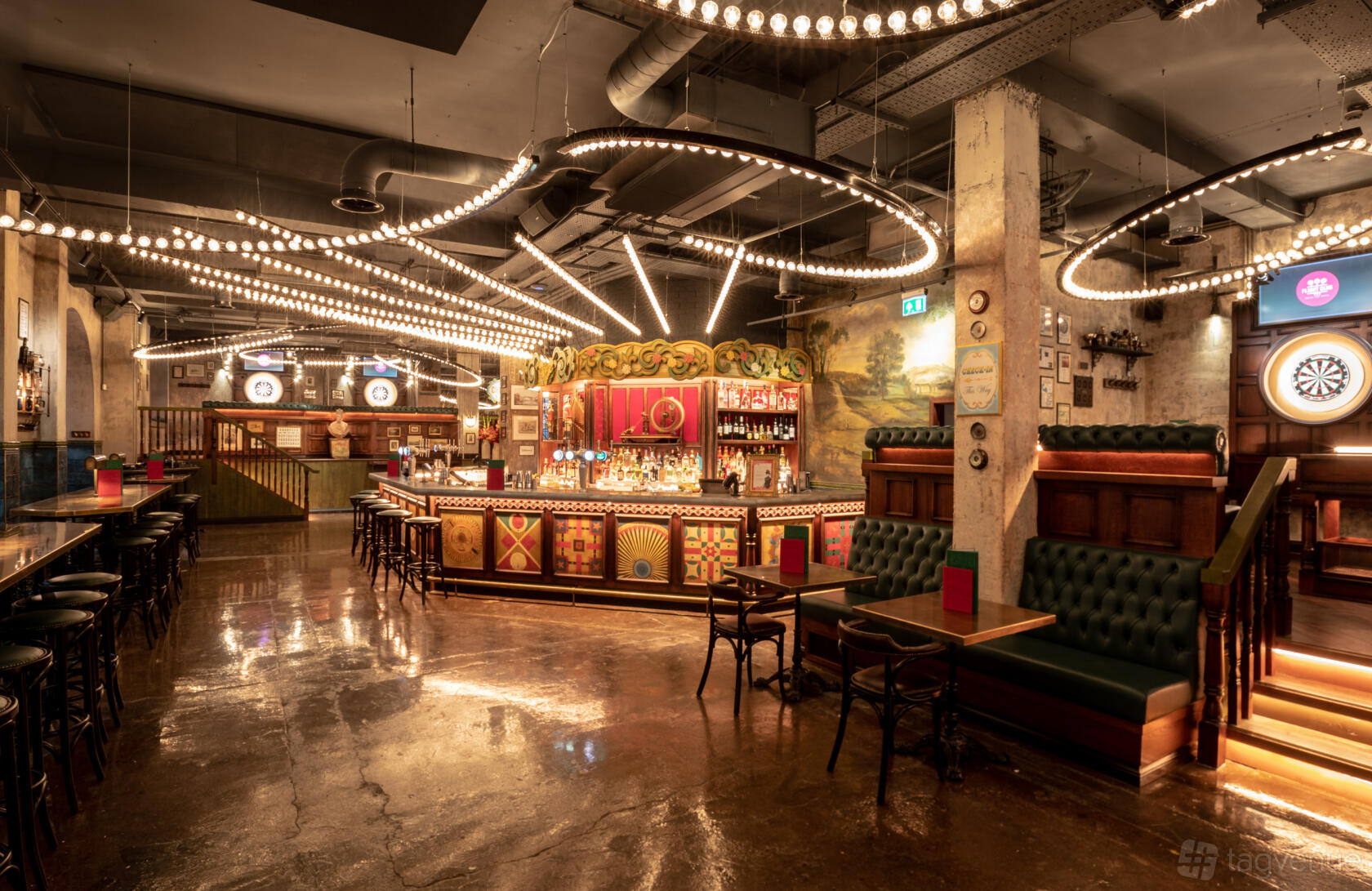 A bar with circular hanging lights, a decorative central bar counter, and green tufted banquettes at Flight Club Manchester.