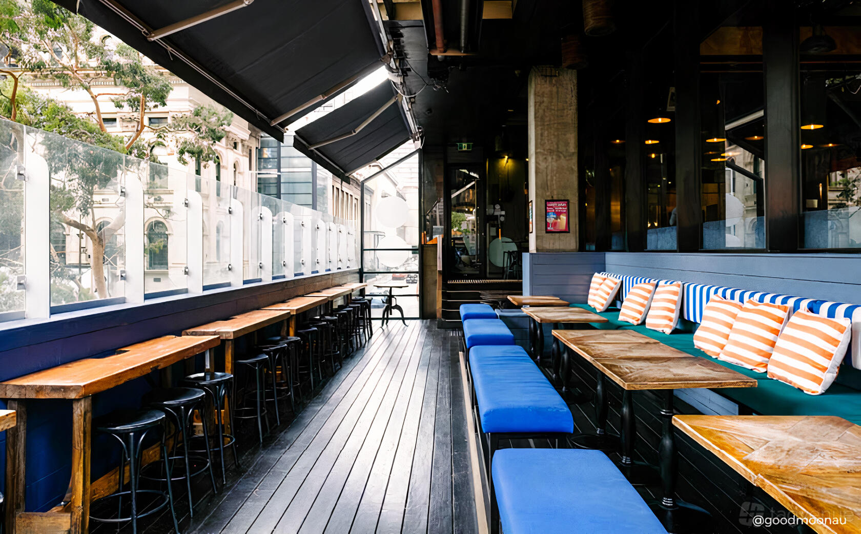 An outdoor dining area with wooden tables, blue cushioned benches, and striped pillows at Father's Office.