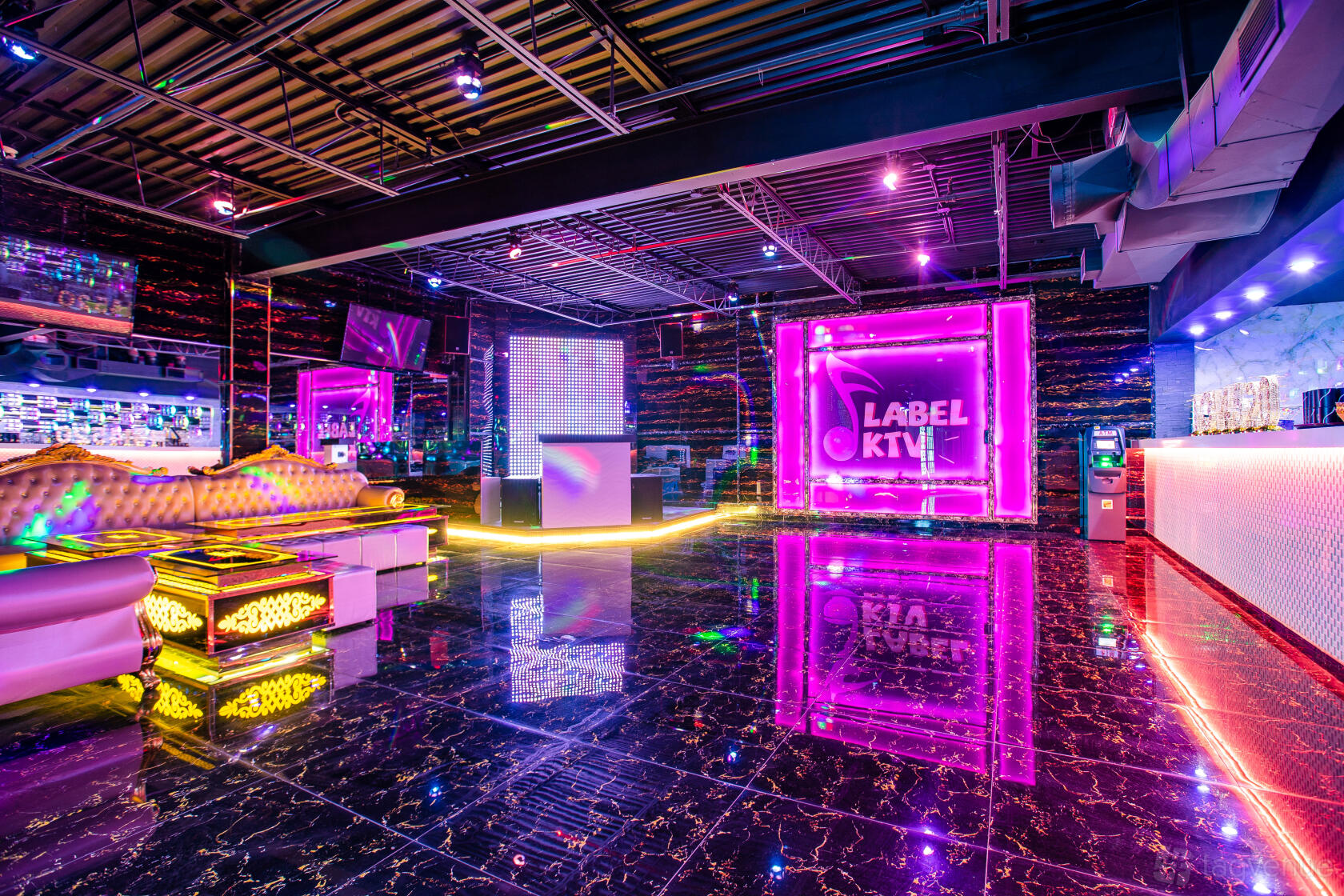 An event space in a karaoke bar with a DJ booth, neon lights, mirrored walls, and glossy tiled floors at Label KTV.