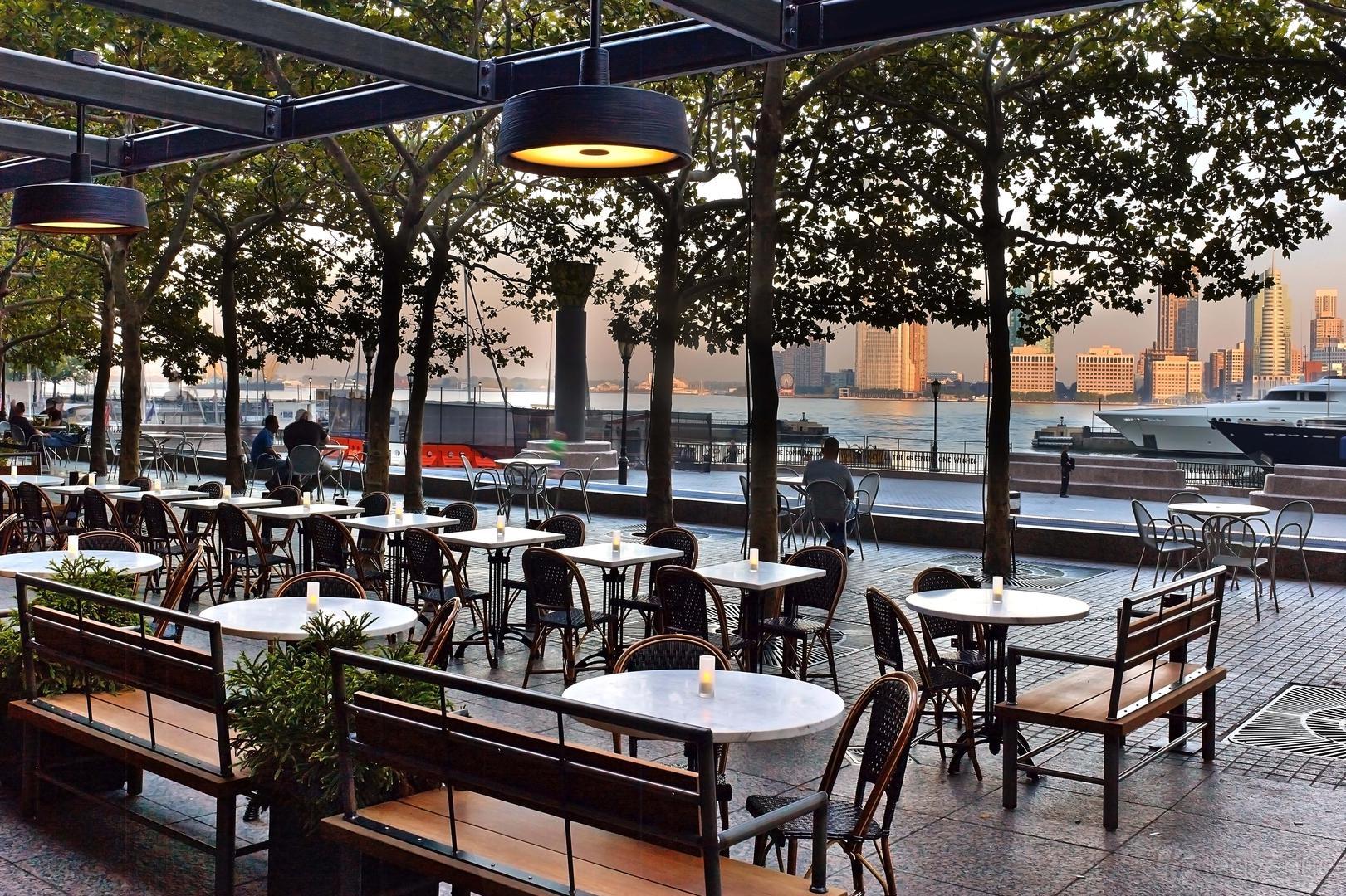 A restaurant terrace with round marble tables, wooden benches, and waterfront views at Le District.