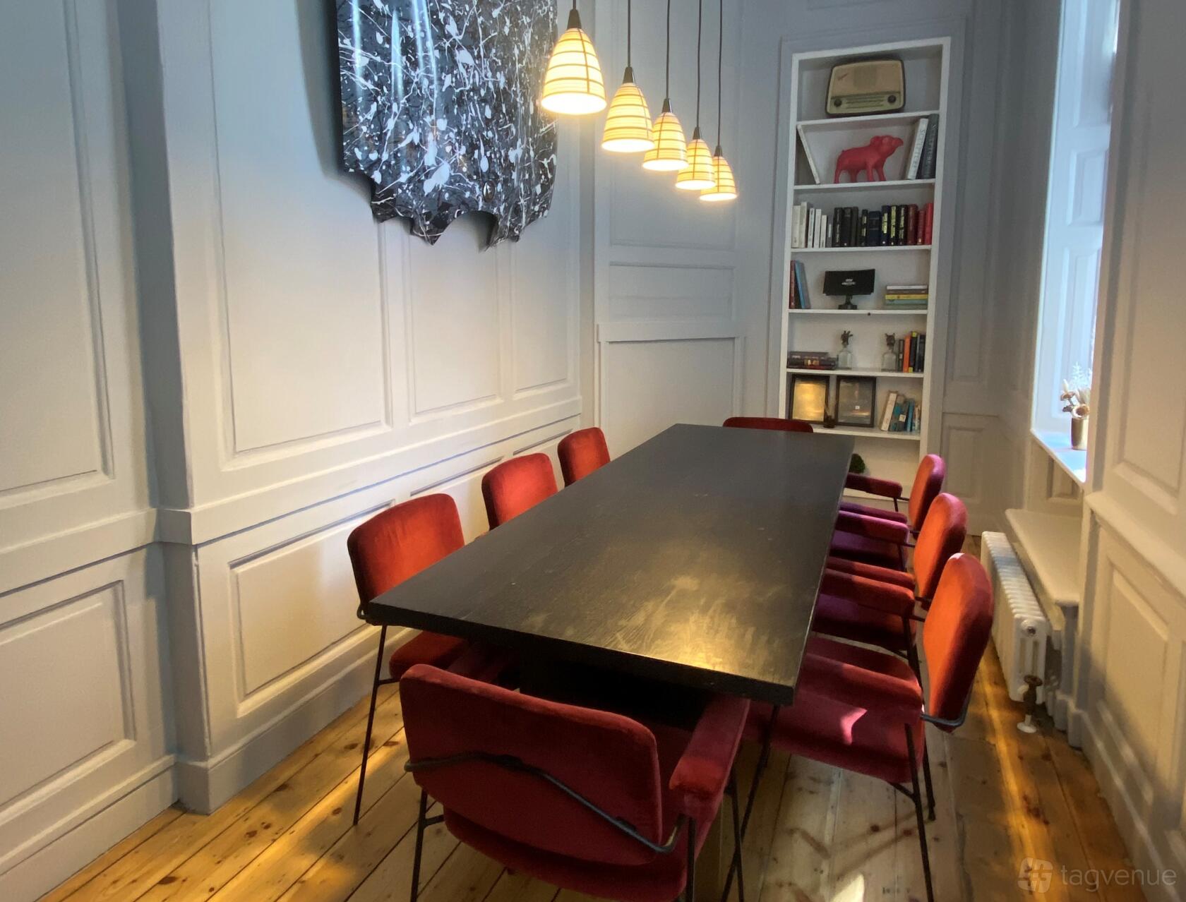 A boardroom with a long dark table, red velvet chairs, and pendant lighting at Electric Space.