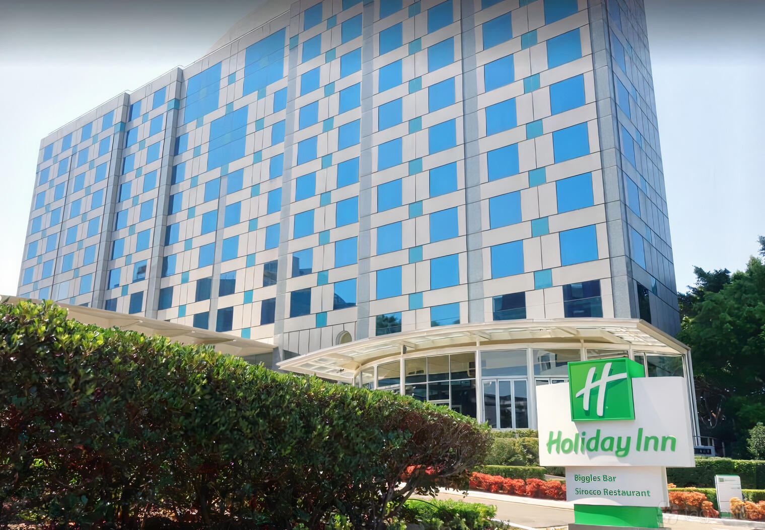 A hotel exterior with a glass facade, geometric windows, and landscaped greenery at Crowne Plaza Sydney Airport.