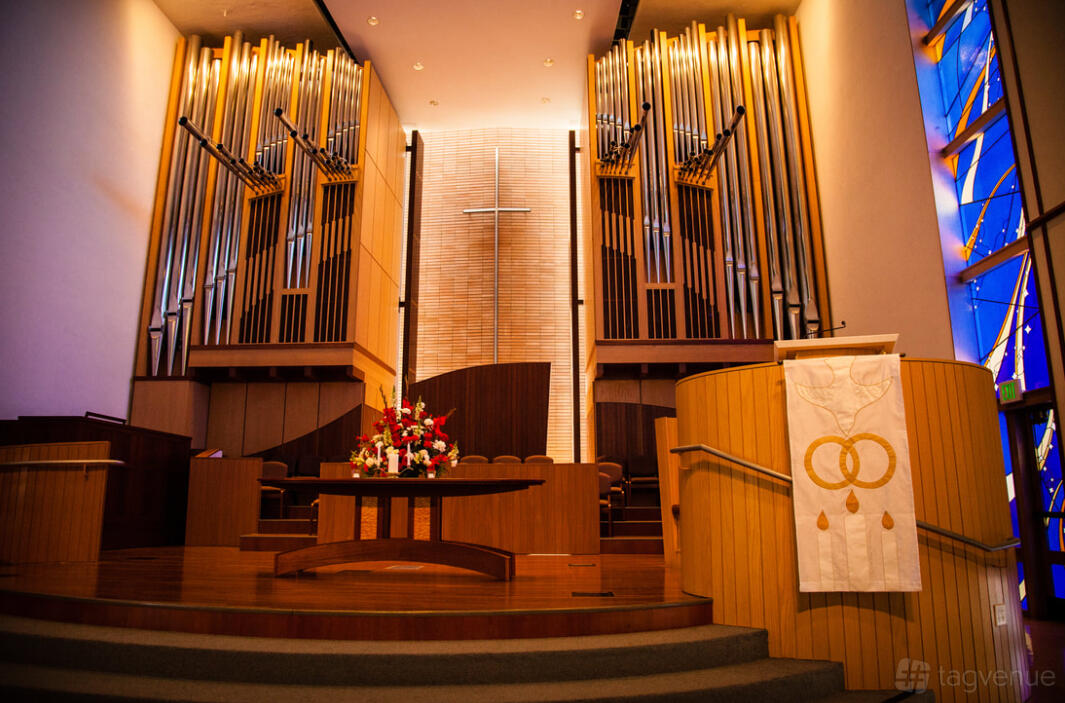 A hall with a raised stage, large pipe organ, wooden paneling, and a cross at Harmony Hall & Courtyard.
