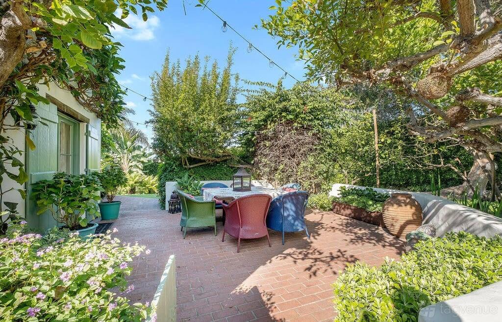 A brick patio surrounded by lush greenery, colorful outdoor seating, and string lights at Ocean View Pool Estate.