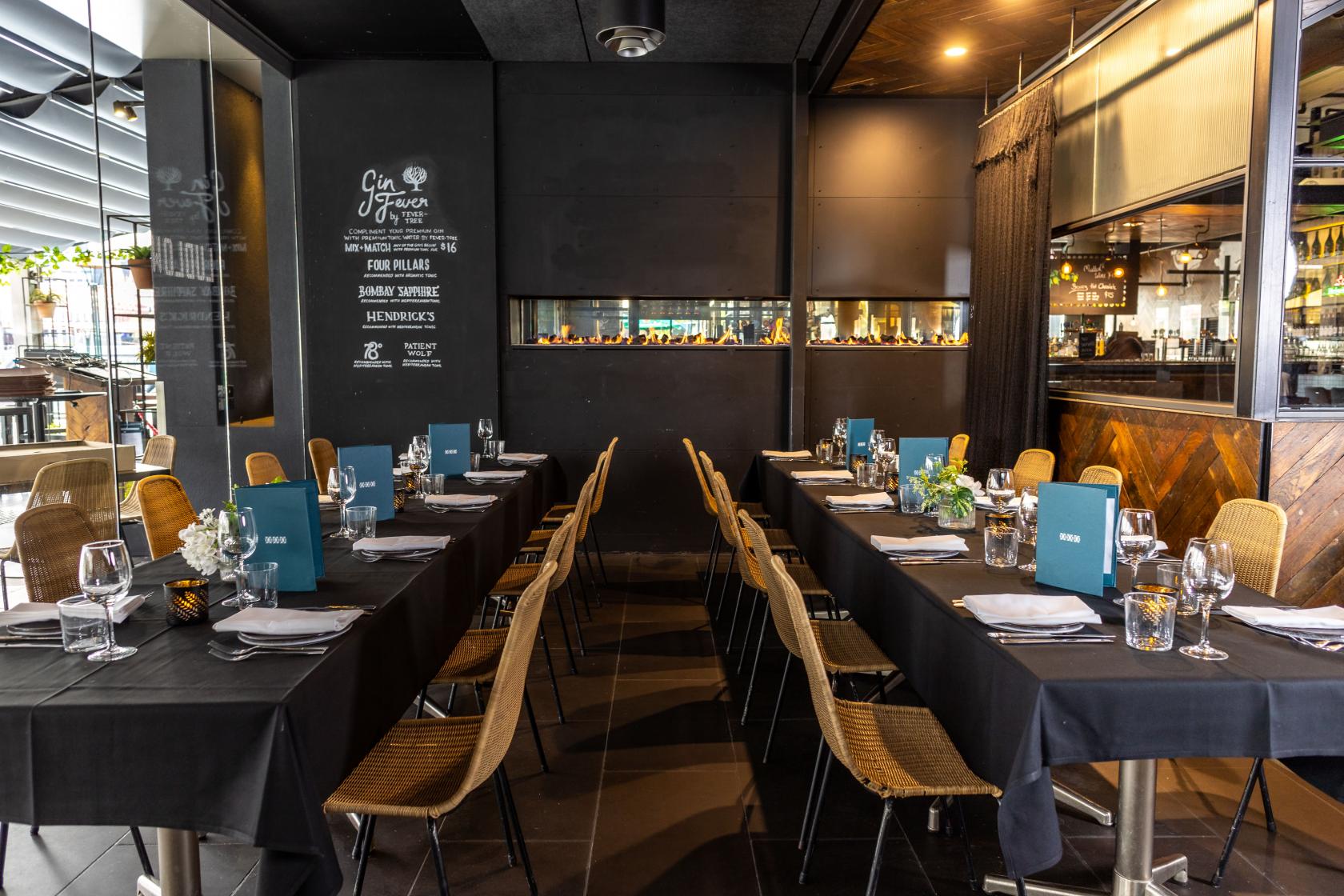 A dining room in a pub with two long tables, black tablecloths, woven chairs, and glassware at Ludlow Bar.