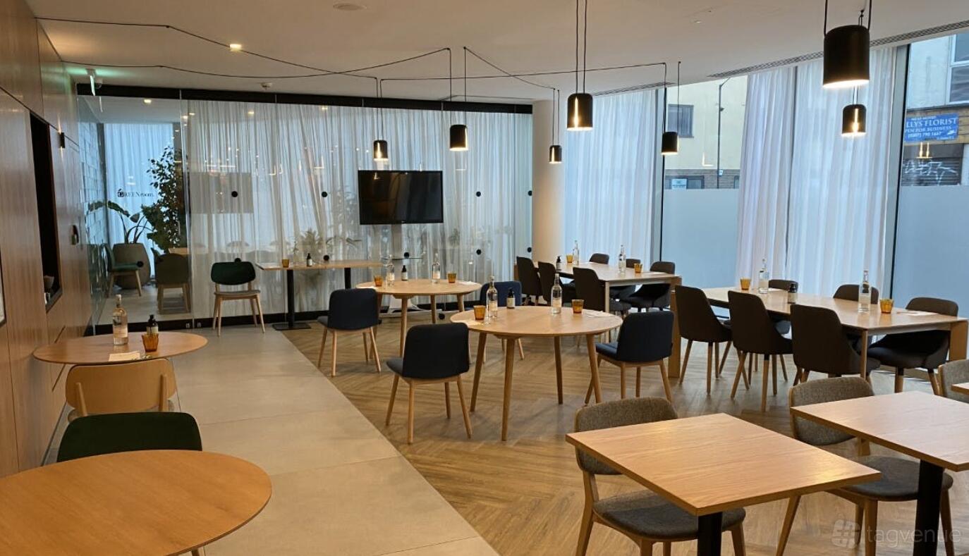 A restaurant with wooden tables, mid-century chairs, pendant lighting, and floor-to-ceiling sheer curtains at Holiday Inn London Whitechapel.