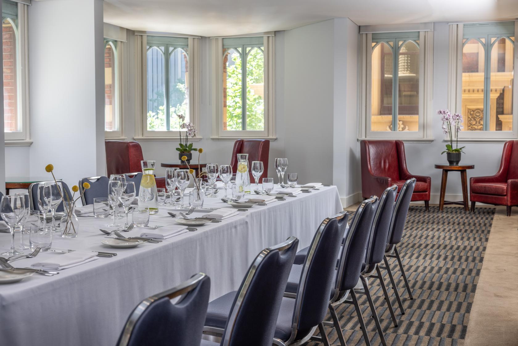 A function room with long tables dressed in white linens, wine glasses, and red armchairs by tall windows at InterContinental Melbourne.