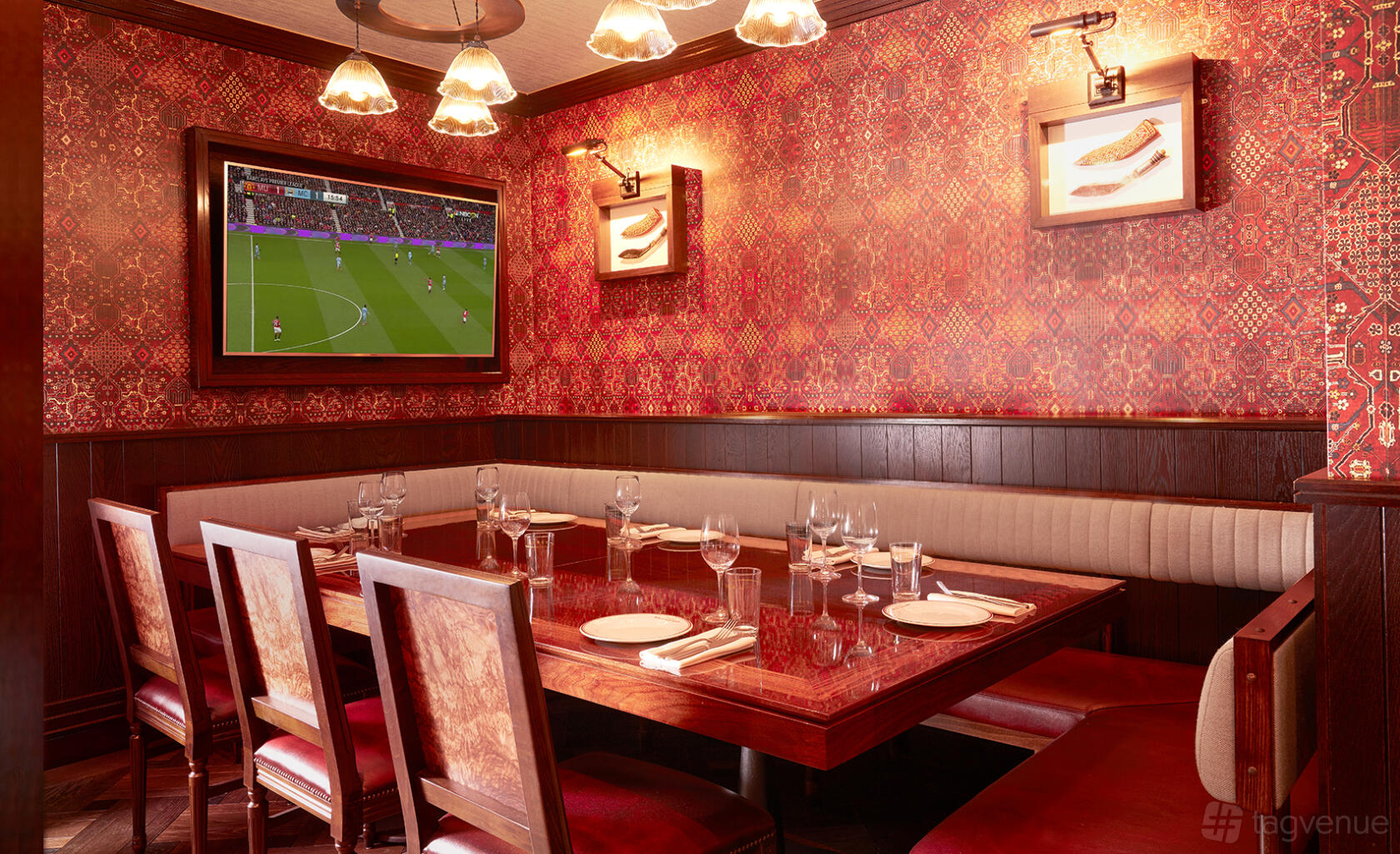 An event space in a restaurant with patterned red wallpaper, a wall-mounted TV, and a wooden dining table at Brigadiers.