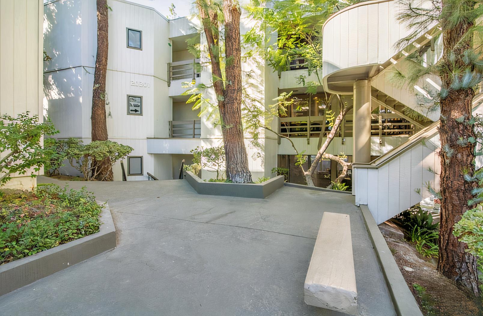 An outdoor film and photo studio with a concrete courtyard, mature trees, and spiral staircase at Evolve Healthcare.