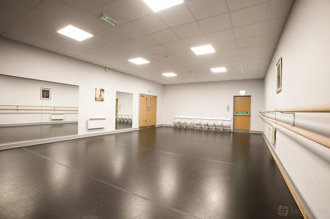 A dance studio with full-wall mirrors, ballet barres, and a row of white chairs at Adagio School Of Dance.