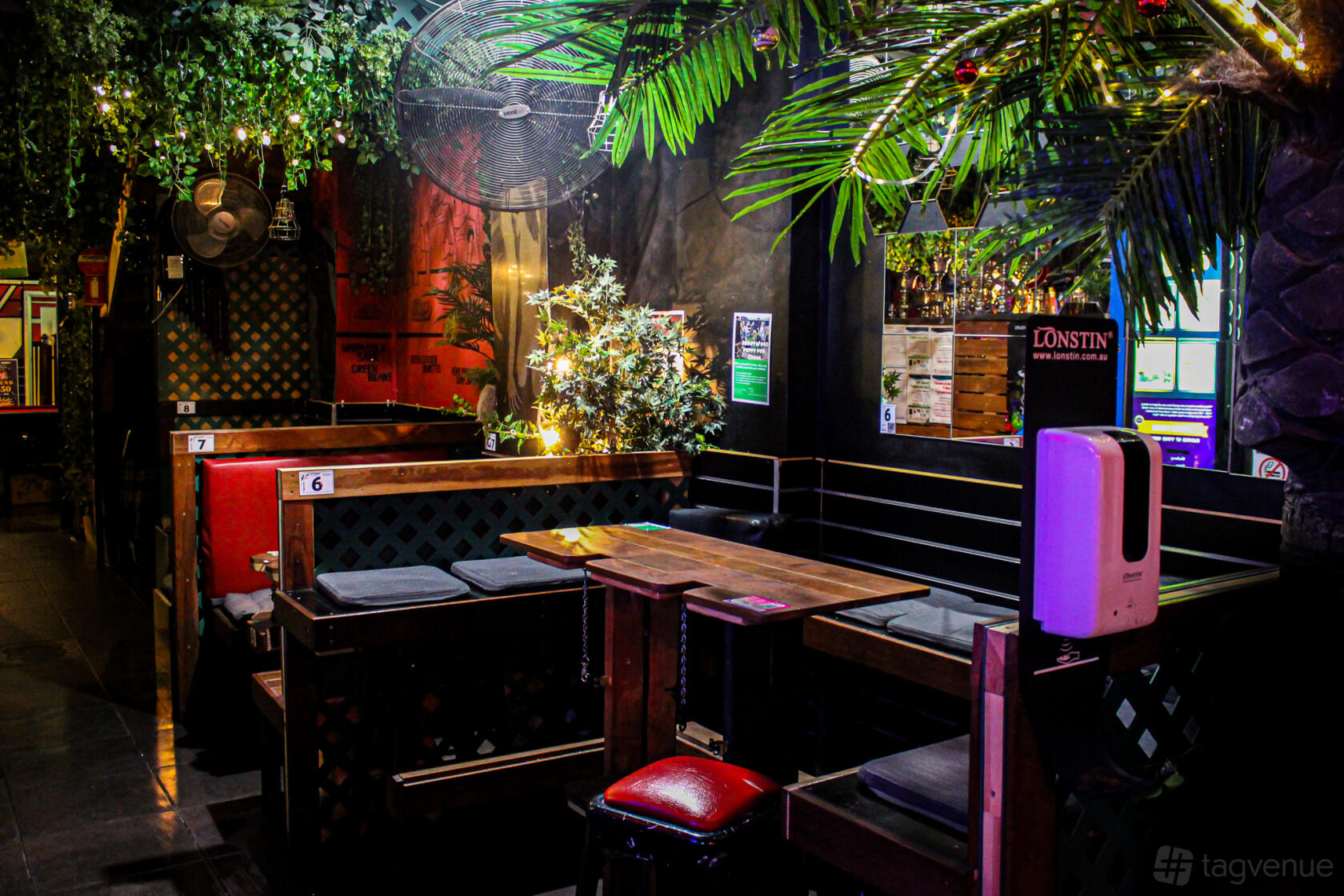 An event space in a bar with booth seating, wooden tables, and hanging greenery at Two Hands Rooftop Bar.