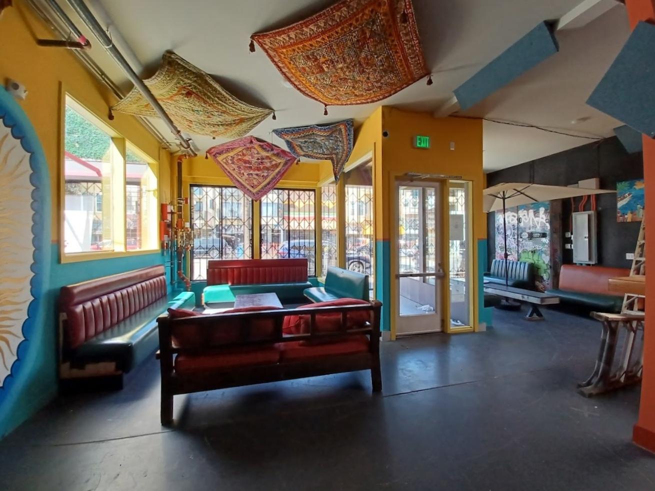 A function room with colorful walls, patterned rugs hanging from the ceiling, and red leather seating at Bissap Baobab.