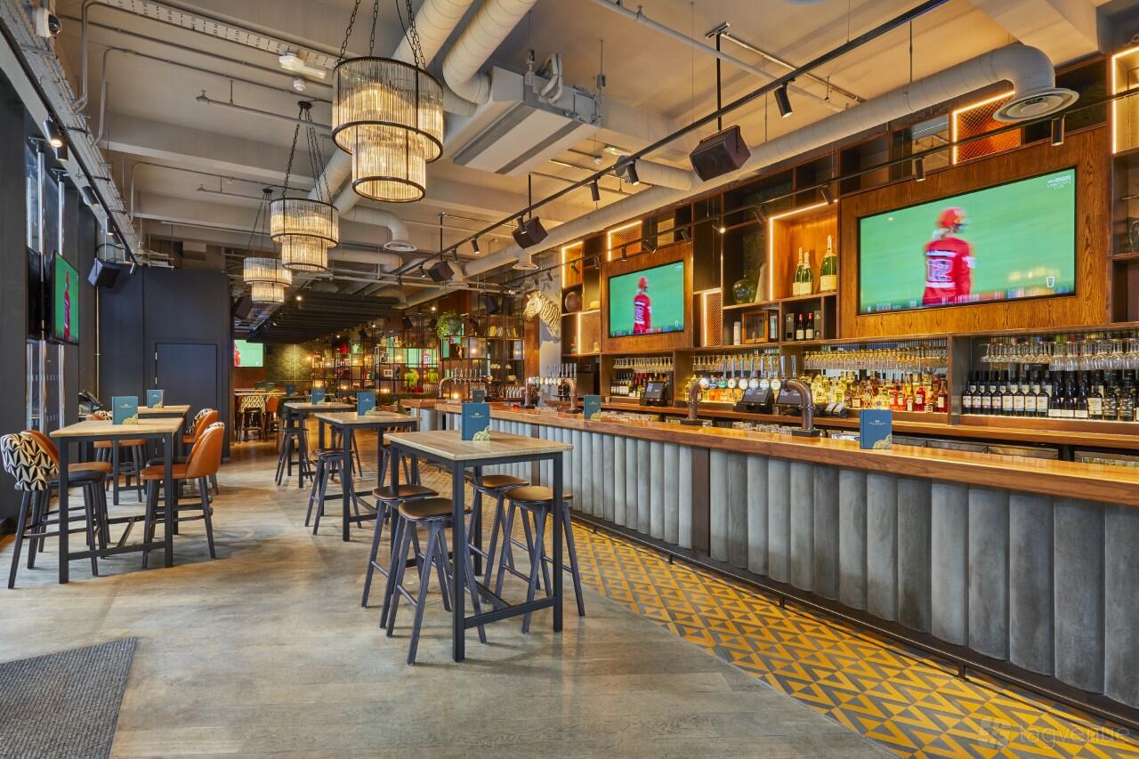 A spacious pub with high tables, pendant chandeliers, multiple TVs, and an extensive bar at Beechwood.