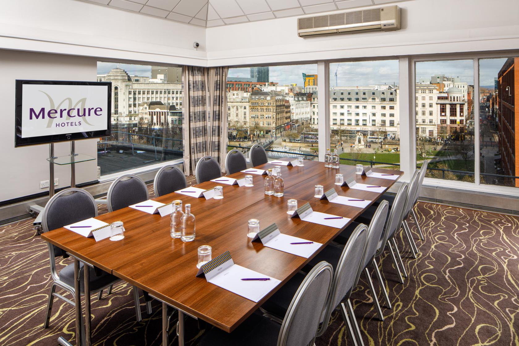 A function room with a large boardroom table, city views through floor-to-ceiling windows at Mercure Manchester Piccadilly.