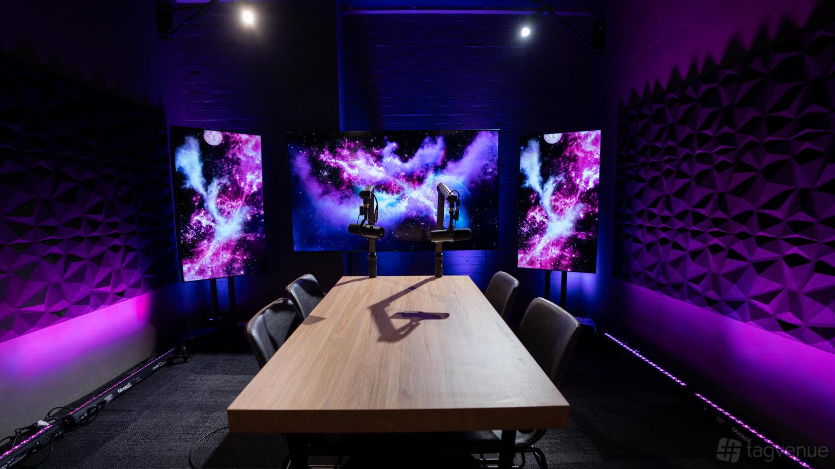 A recording room with a wooden table, podcast microphones, and acoustic foam panels at The Media Joint.