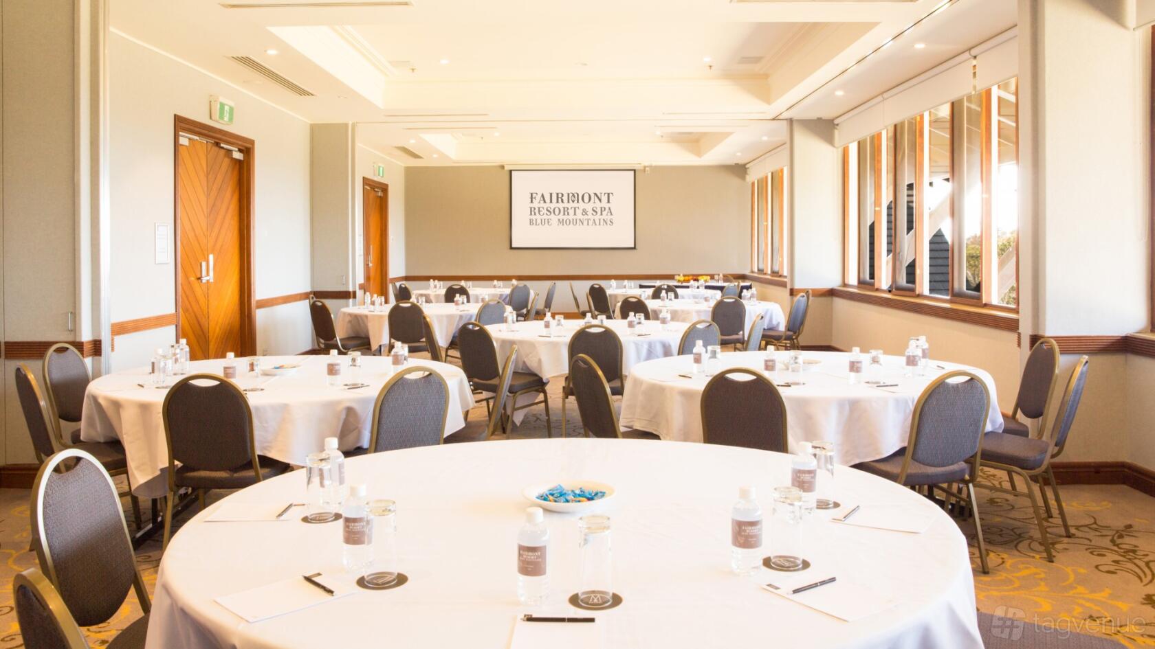 A hotel conference room with round tables set with water bottles and chairs at Fairmont Resort Blue Mountains.