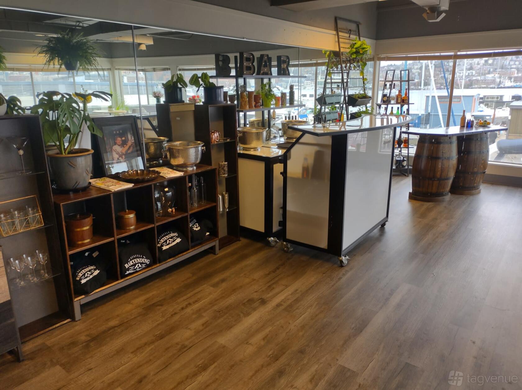 An event venue with a wooden floor, mobile bar stations, and large windows overlooking the water at Seattle Bartending Co.